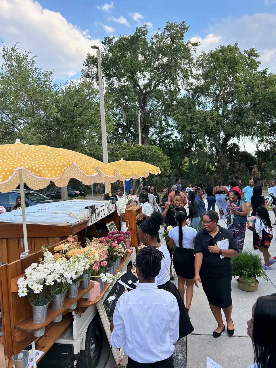 A crowd of guests at the flower truck’s bouquet bar under yellow polka-dot umbrellas on a sunny day