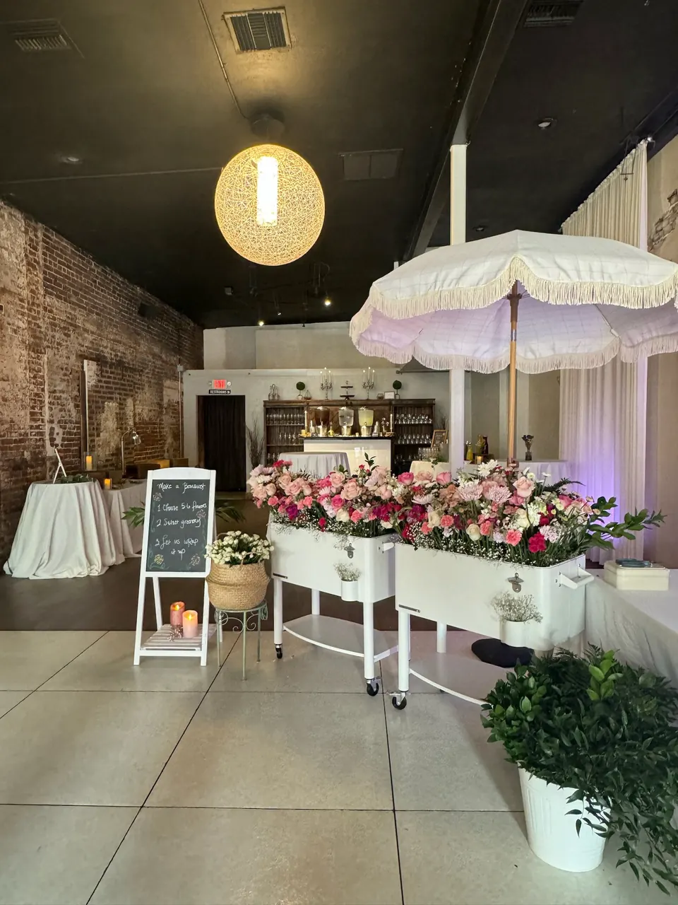 Indoor flower bar: two carts of pink and red blooms under a fringed umbrella with a make-a-bouquet chalkboard