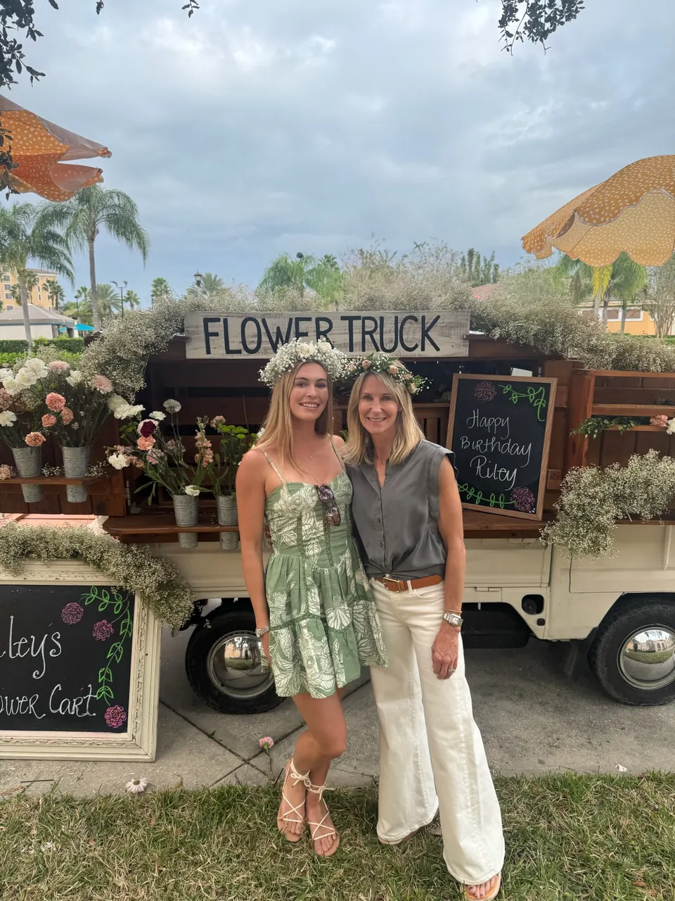 Two smiling guests holding bouquets in front of the flower truck on a sunny day